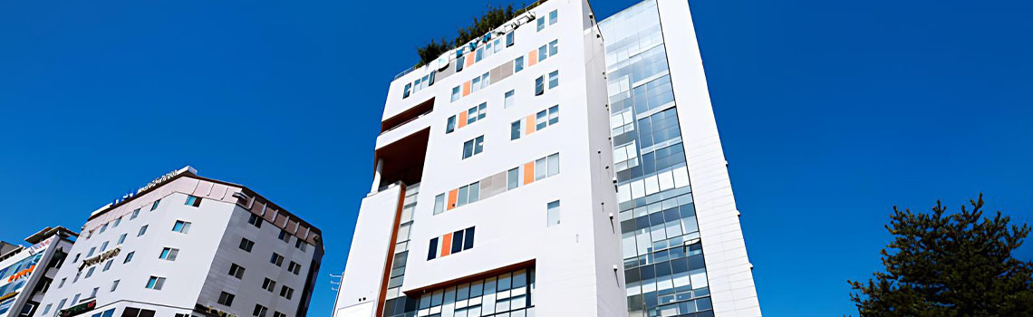 A tall, modern white hospital building with orange accents and large glass windows under a clear blue sky in Namyangju.