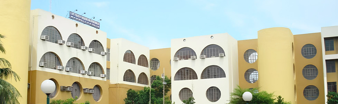 One Indian school building with arched and circular windows, yellow and white facade, lush greenery, and clear blue sky.
