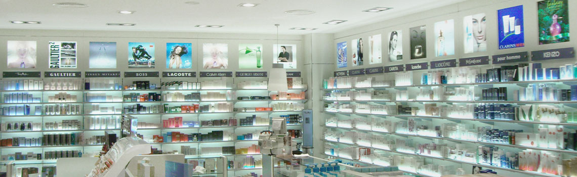 Interior of a brightly lit perfume store with white shelves organized by brand and illuminated advertisement displays.