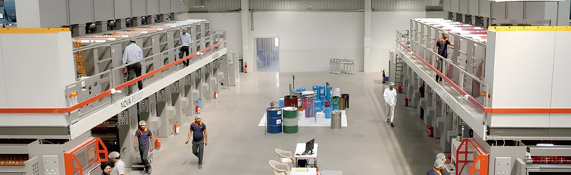 Workers operate large-scale printing and packaging machines inside a modern Indian printing and packaging factory